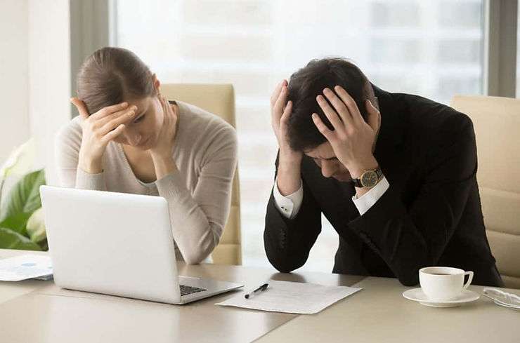 Two frustrated coworkers working on laptop.